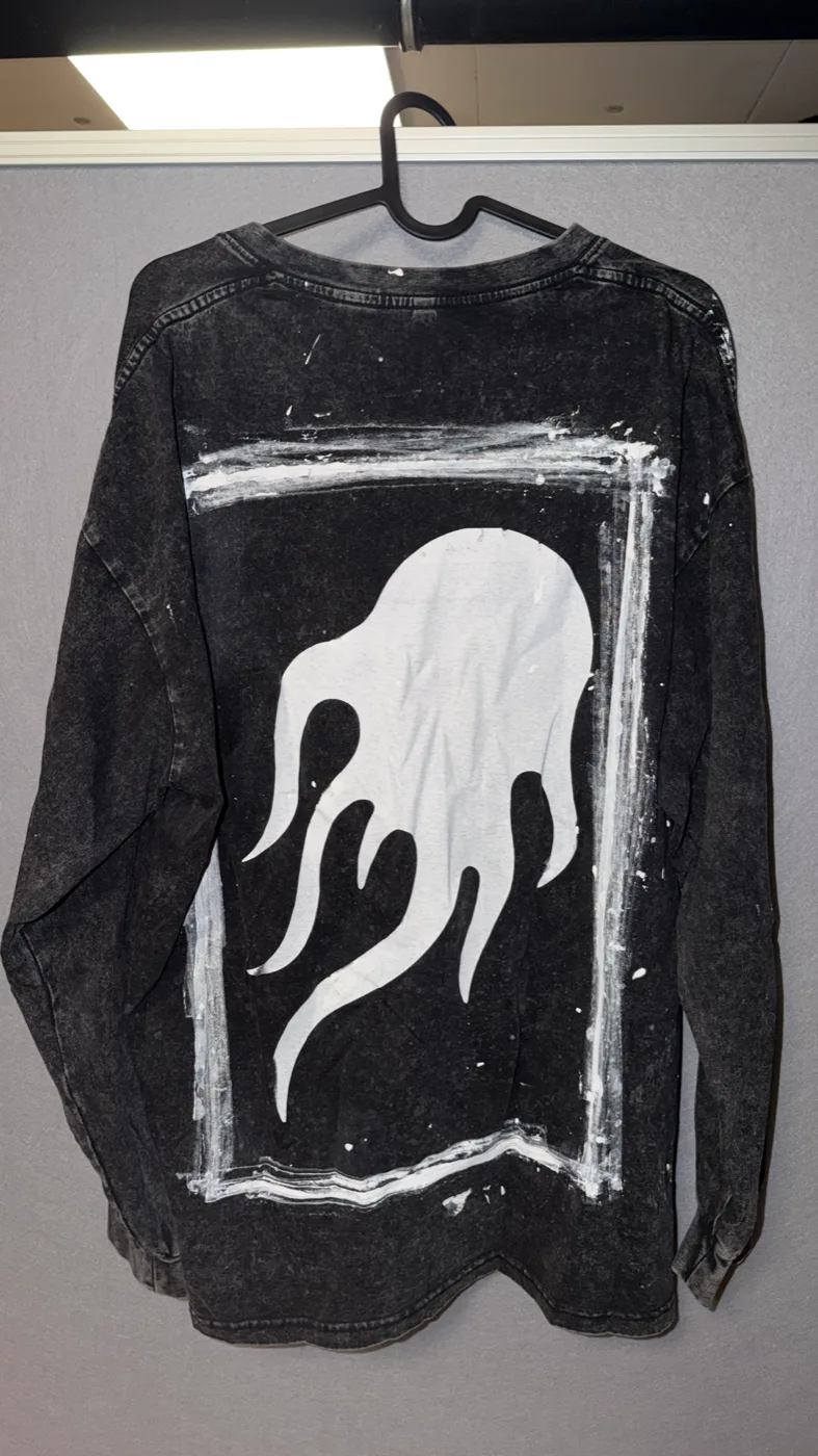 A black long-sleeve shirt hand-painted with a white flame, hanging on a rail.