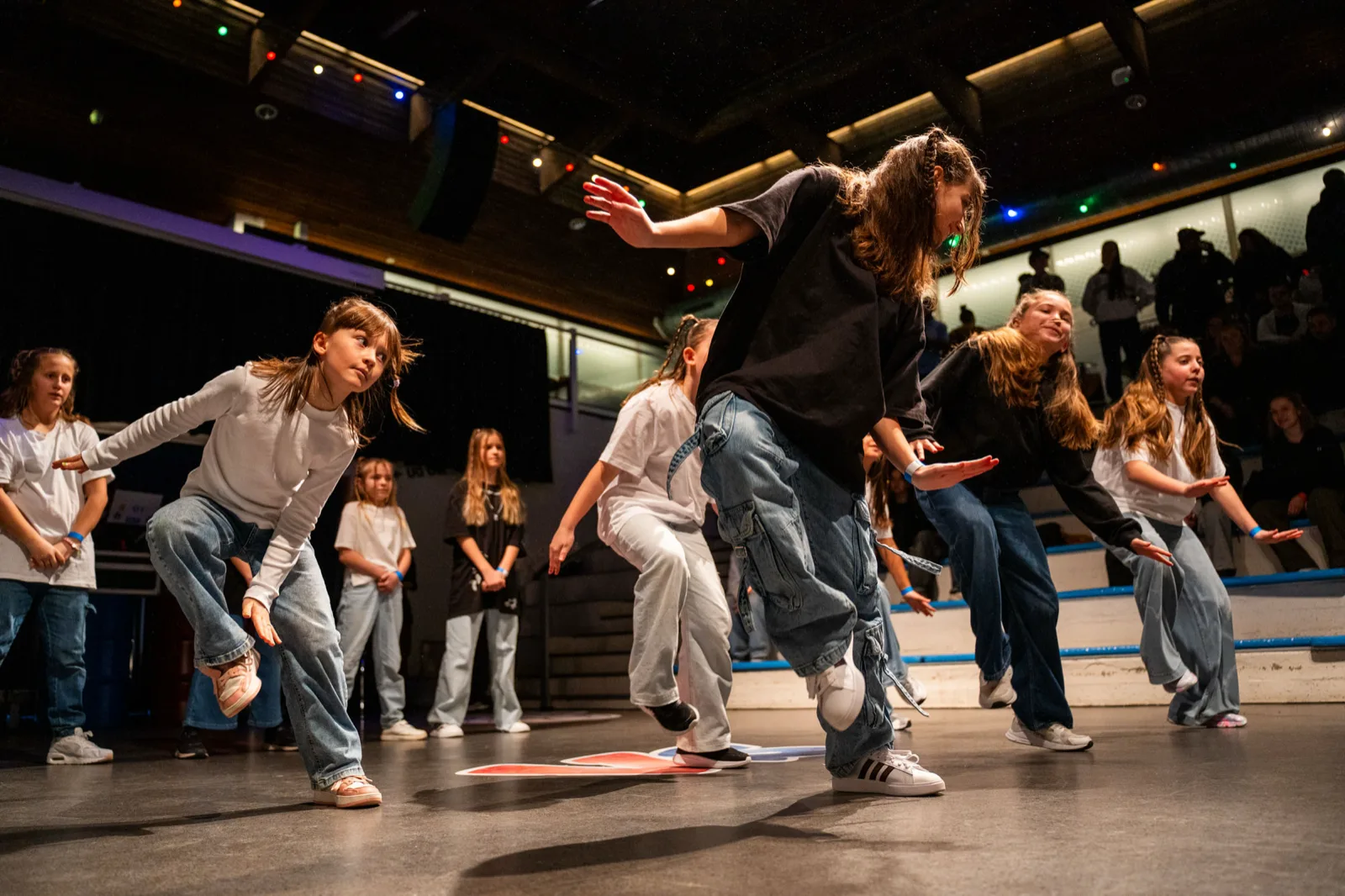 The kids group mid-routine on a lit stage, arms out, the audience in the dark behind.