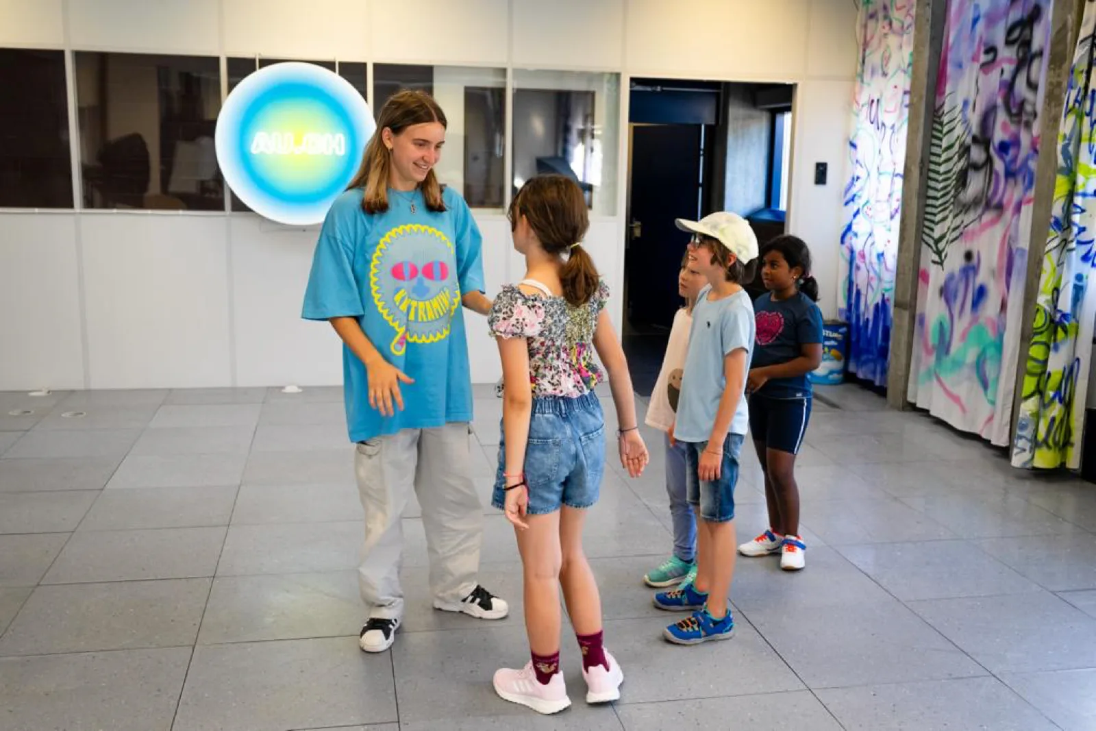 A teacher in an AUCH shirt talking to four children in the studio.