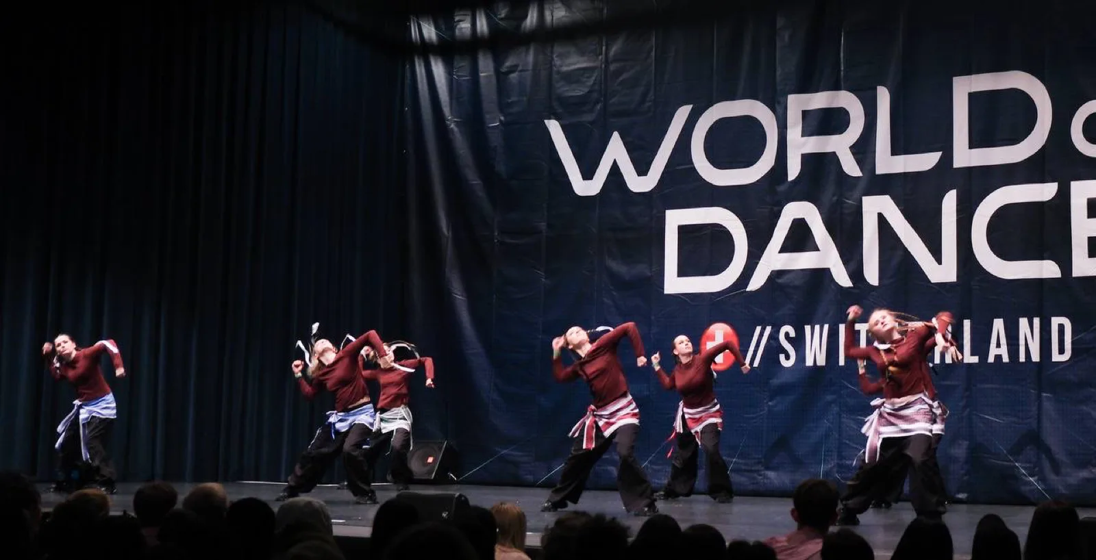 The team mid-phrase on stage in front of a World of Dance Switzerland banner.
