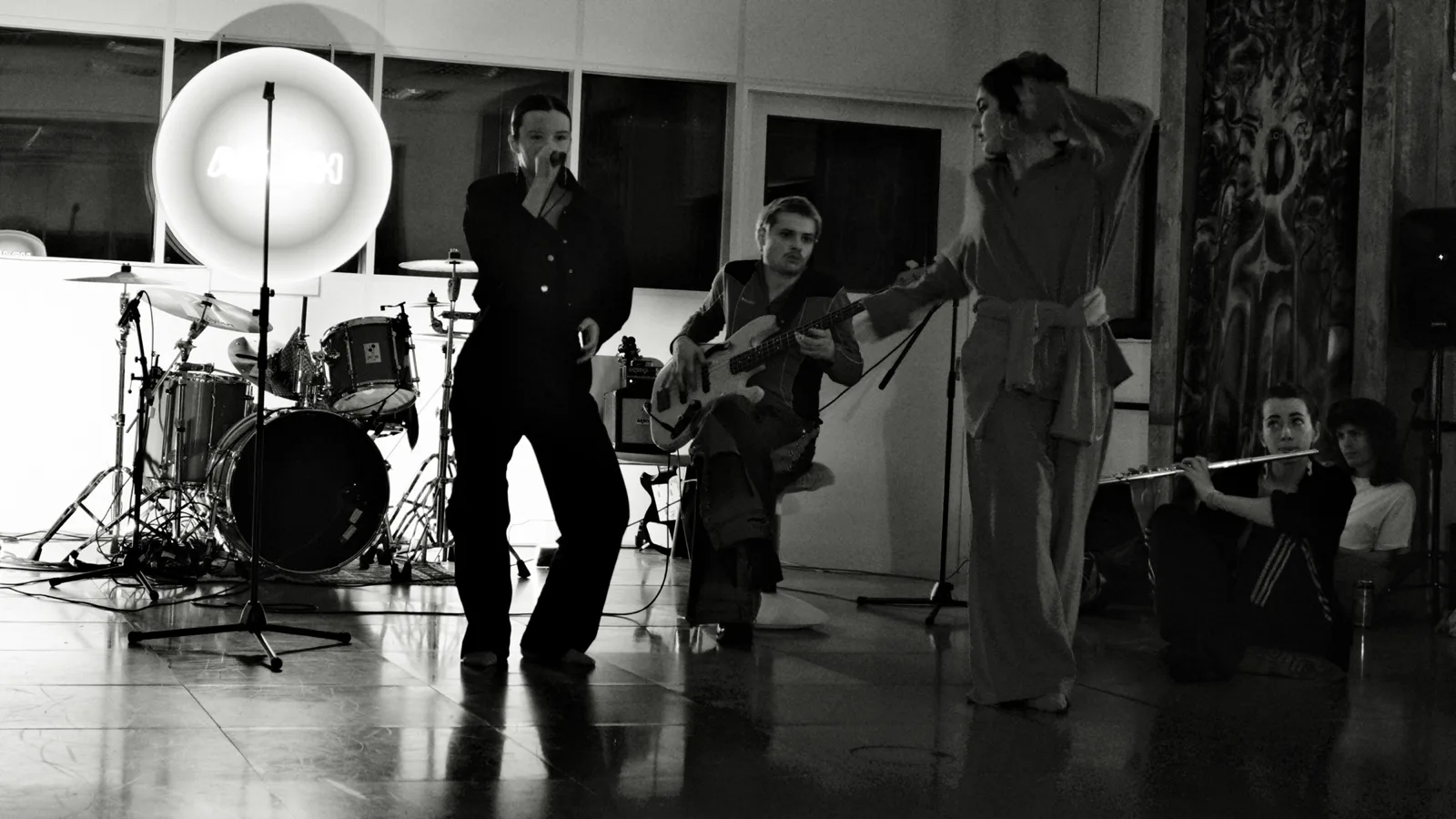 A singer, bass player and flautist performing in the studio, photographed in black and white.