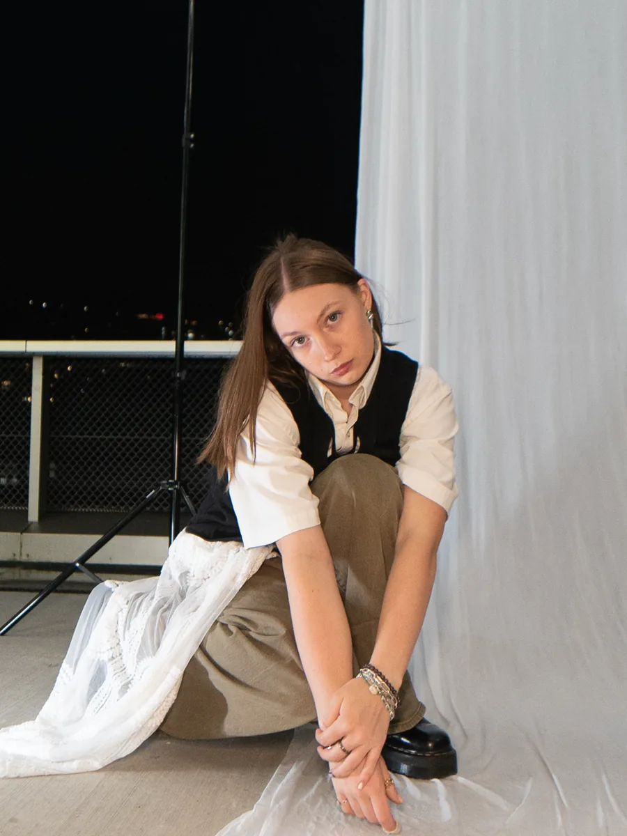 Kristina sitting against a white drop on a rooftop at night.